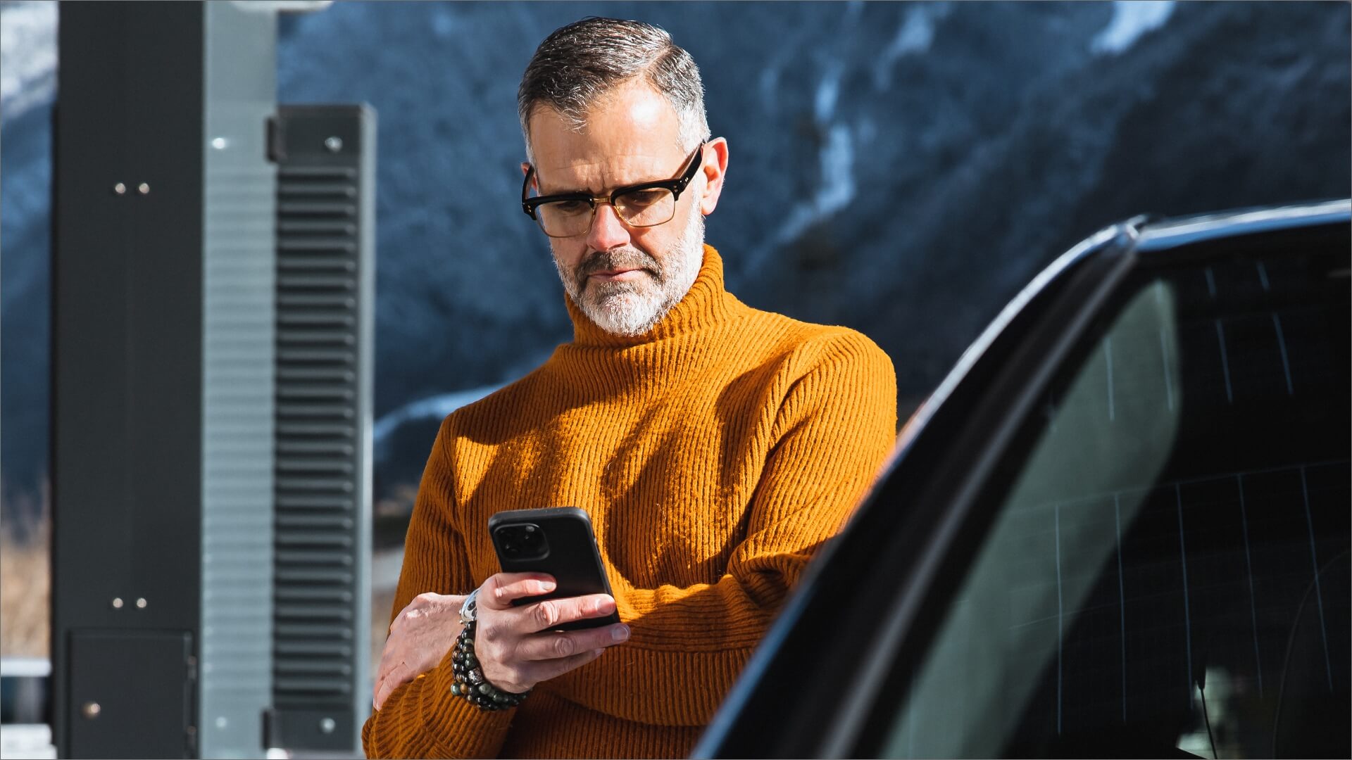 Mann mit Smartphone lädt Elektroauto